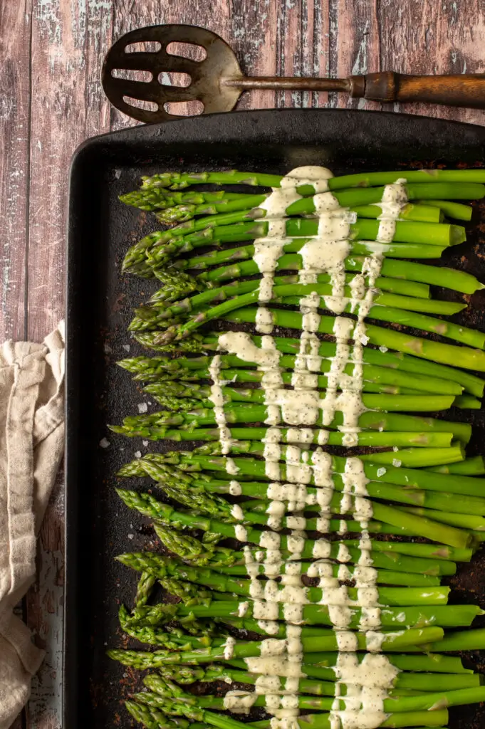 vegan lemon poppyseed drizzled over asparagus on baking sheet