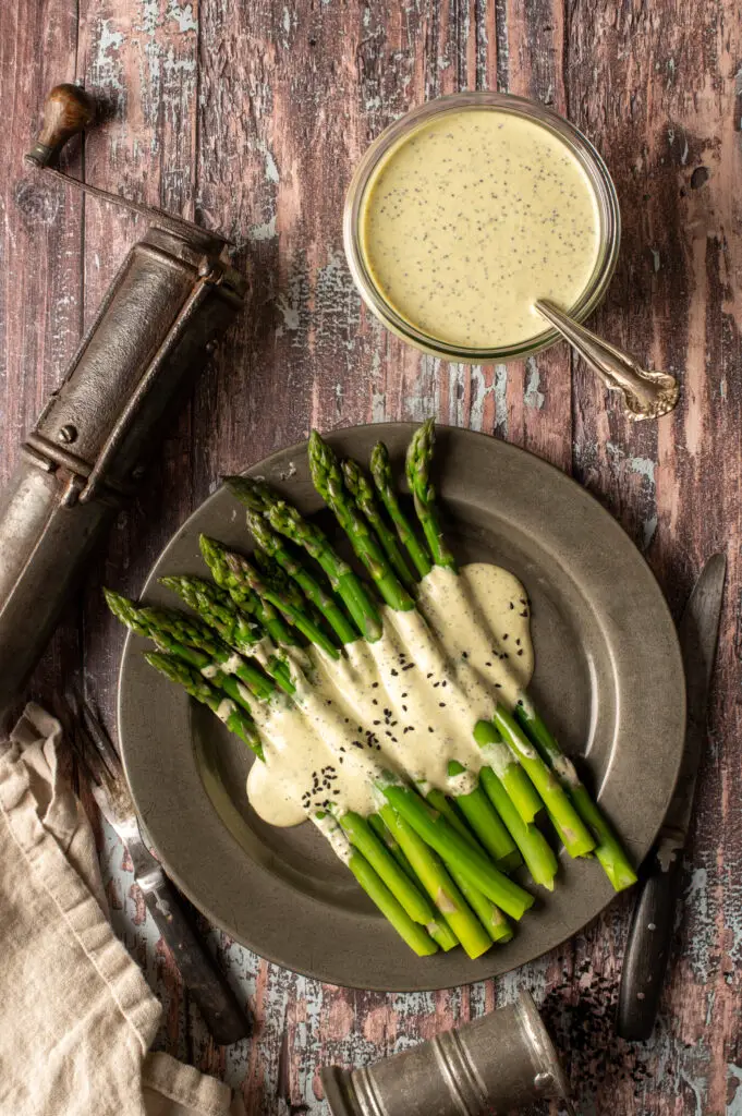 vegan lemon poppyseed drizzled over asparagus on pewter plate next to jar of dressing