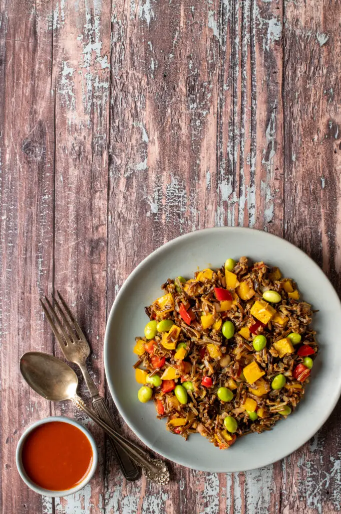 wild rice and mango salad on plate next to hot sauce in small bowl