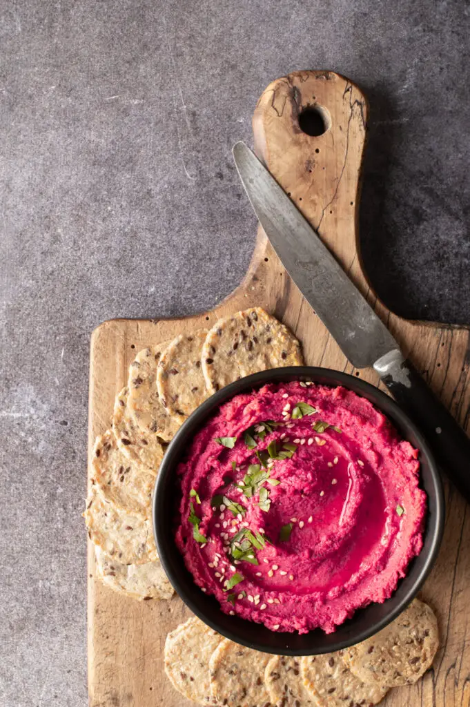 beet and dill hummus in black bowl on cutting board with crackers