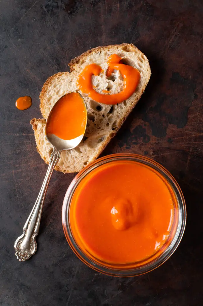 cayenne pepper hot sauce in glass jar next to piece of bread with hot sauce drizzled on it