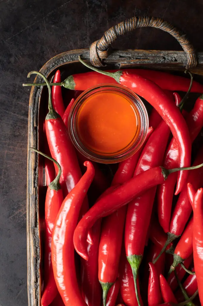 cayenne pepper hot sauce in glass jar in basket filled with fresh cayenne peppers