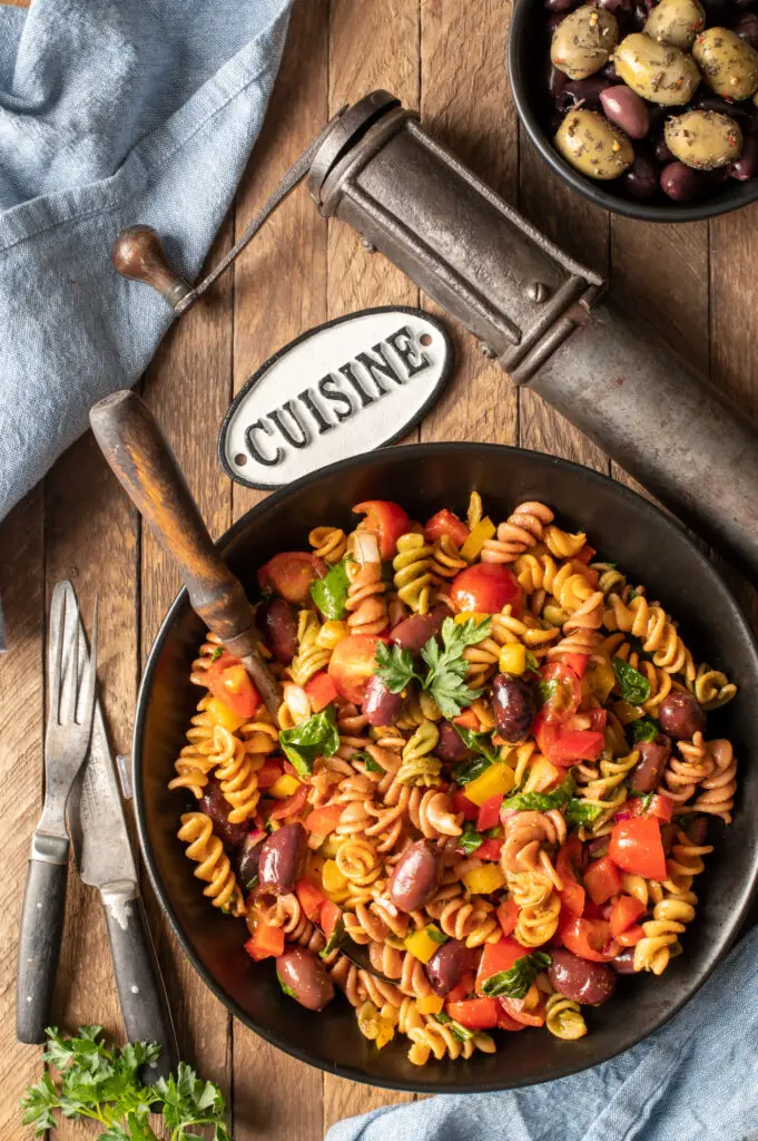 simple italian pasta salad in black bowl next to spice grinder and bowl of olives