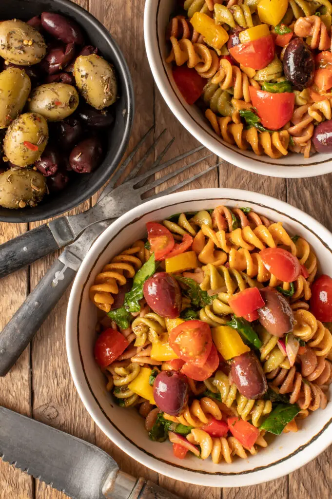 simple italian pasta salad in small white bowls next to bowl of olives