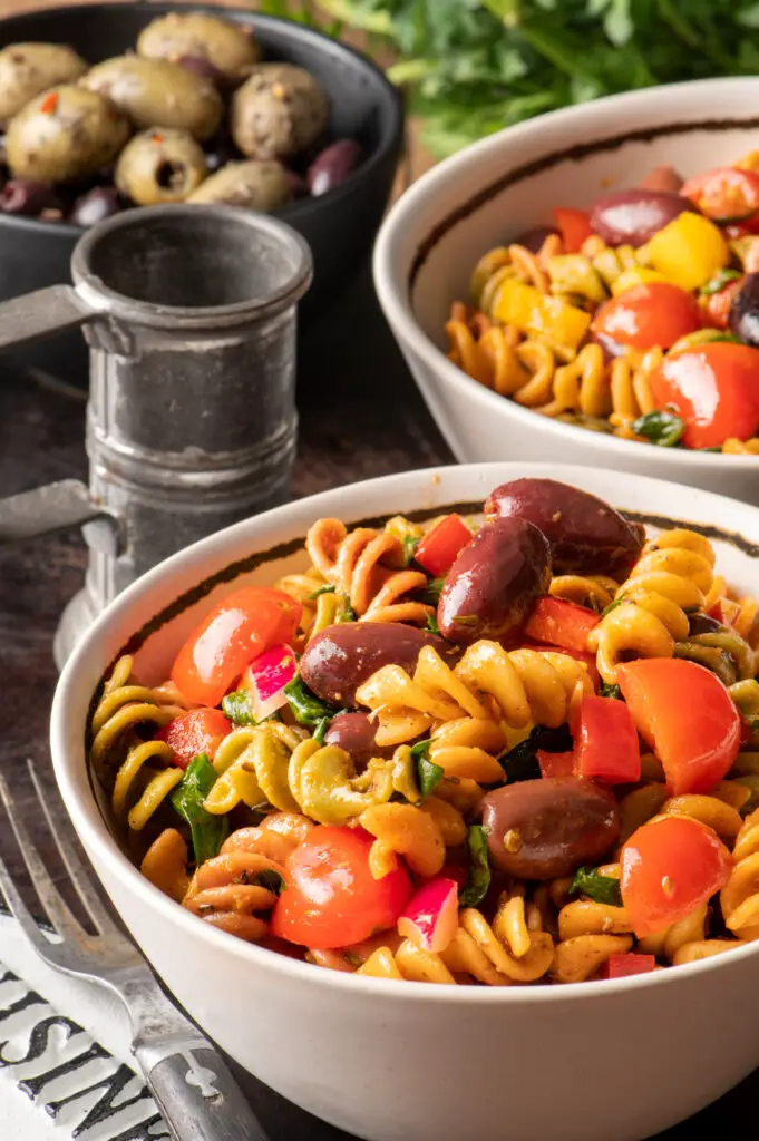 simple italian pasta salad in small white bowls next to bowl of olives