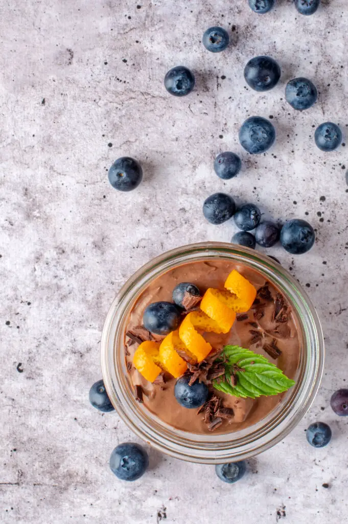 creamy chocolate coconut pudding in jar with blueberries scattered on counter