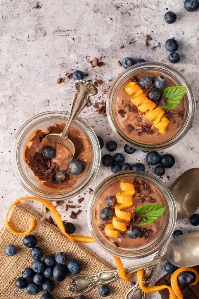 creamy chocolate coconut pudding in jars with blueberries and chocolate shavings scattered around on counter