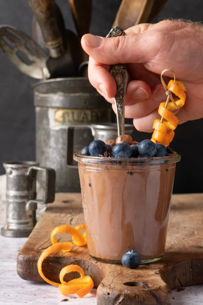 creamy chocolate coconut pudding in jar with hand holding spoon in jar