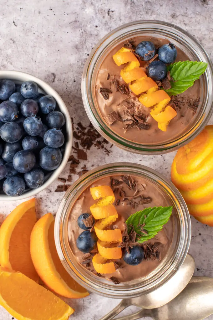 creamy chocolate coconut pudding in jars next to blueberry in dish