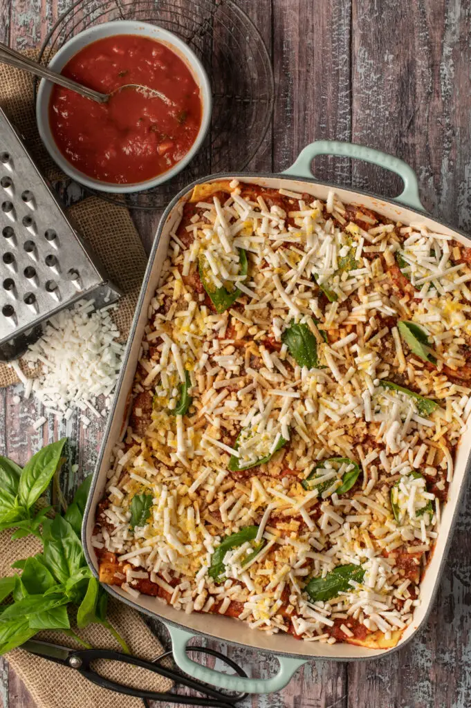 uncooked lasagne in baking pan next to tomato sauce in bowl