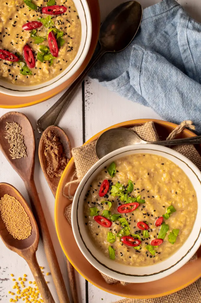 basic mung dal in two white bowls next to spices in wooden spoons