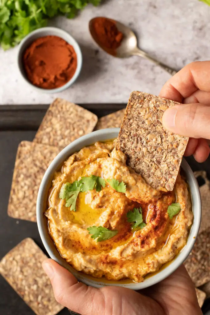 baba ganoush in bowl with hand dipping cracker into bowl