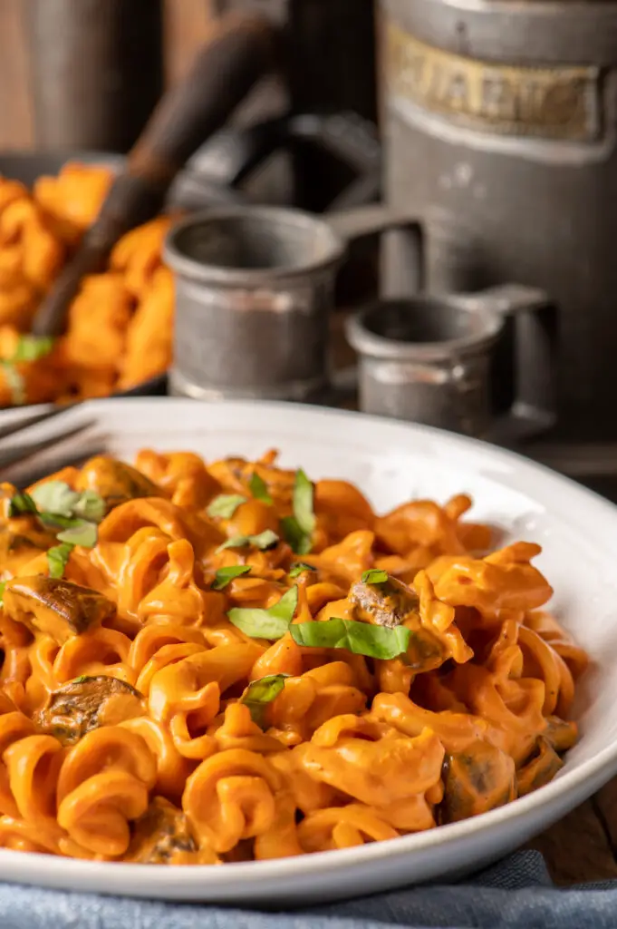 creamy roasted red pepper pasta in white bowl with measuring cups in background