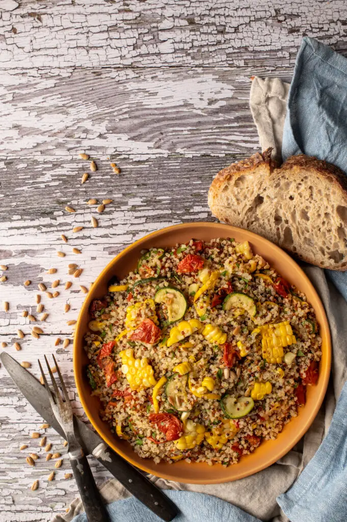 quinoa with summer vegetables on plate next to cutlery and slice of sourdough