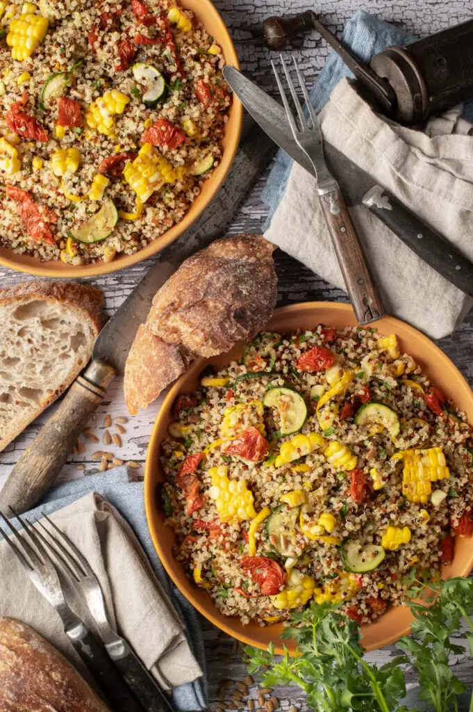 quinoa with summer vegetables on two plates next to cutlery an sourdough slices