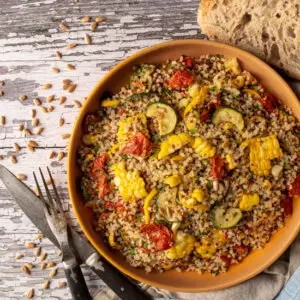 quinoa with summer vegetables on plate next to cutlery and slice of sourdough - recipe image