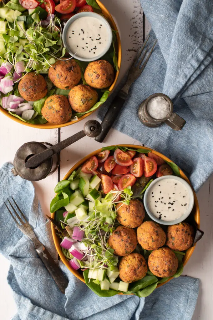 two falafel plates with tomatoes, cucumber and greens