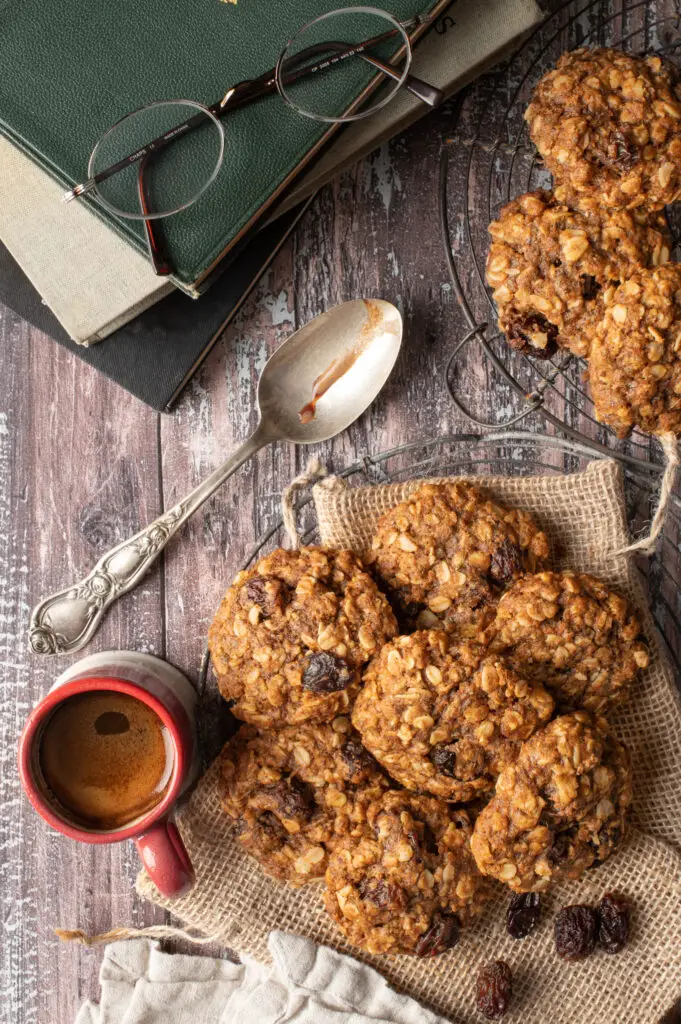 vegan oatmeal raisin cookies on cooling rack next to cup of espresso and old books