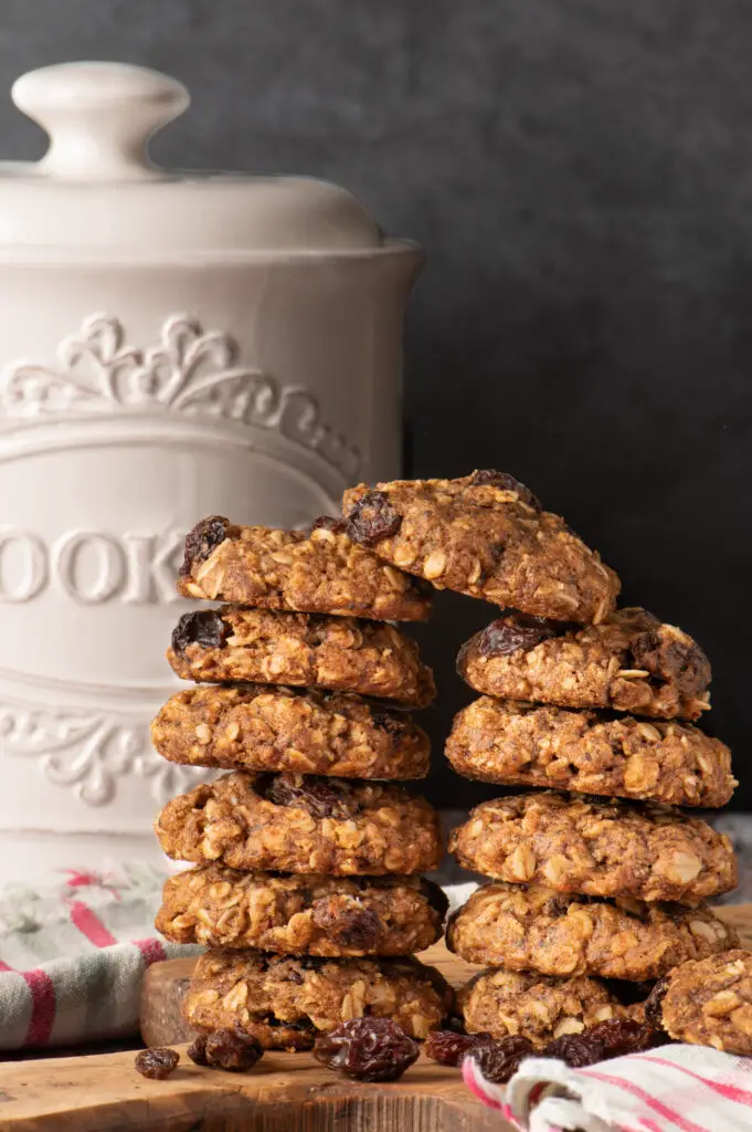 vegan oatmeal raisin cookies on old cutting board with cookie jar in background