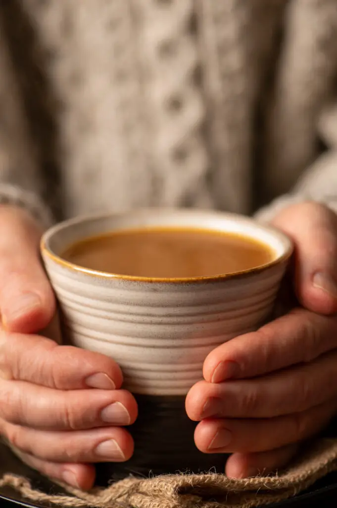 prepared vegetable broth in soup mug held by two hands