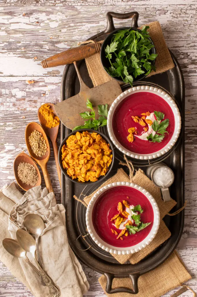 velvety beet soup in two white bowls sitting on cast iron serving tray
