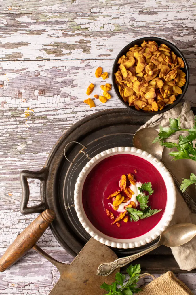 velvety beet soup in two white bowl sitting on cast iron serving tray next to dish of roasted almonds