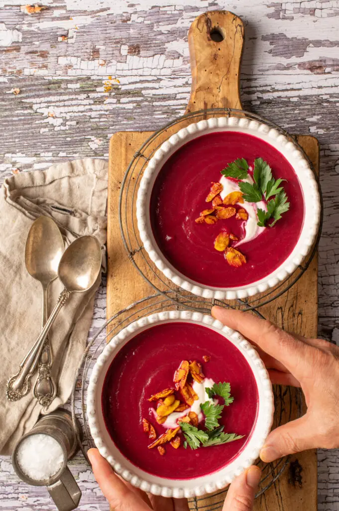 velvety beet soup in two white bowls sitting on cutting board