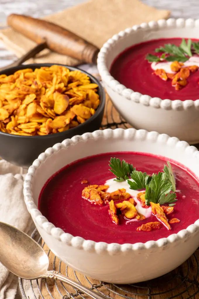 velvety beet soup in two white bowls sitting on cutting board