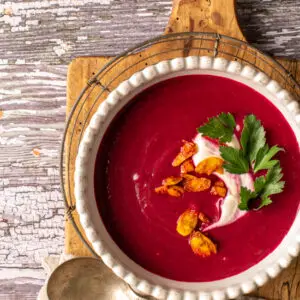 velvety beet soup in white bowl sitting on cutting board - recipe image