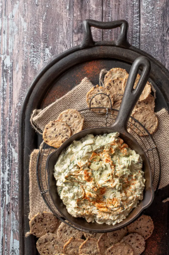 cashew spinach and artichoke dip in iron skillet with crackers on iron tray