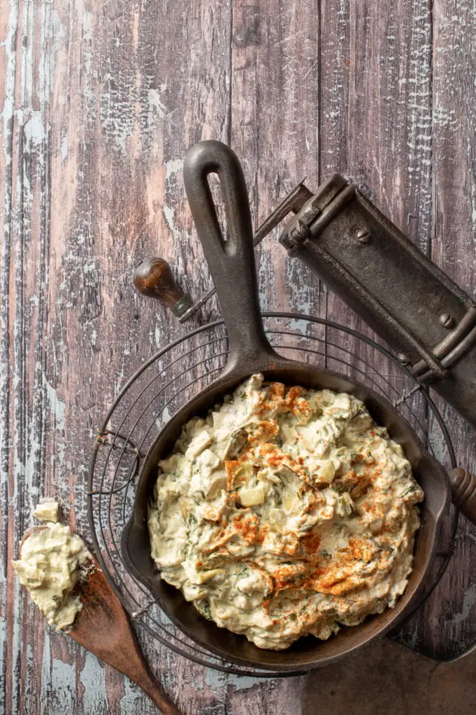 cashew spinach and artichoke dip in iron skillet on cooling rack